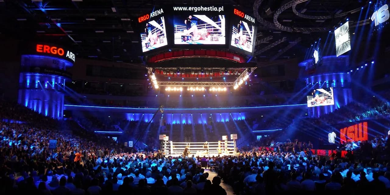 A boxing ring lit up at the centre of a packed indoor arena