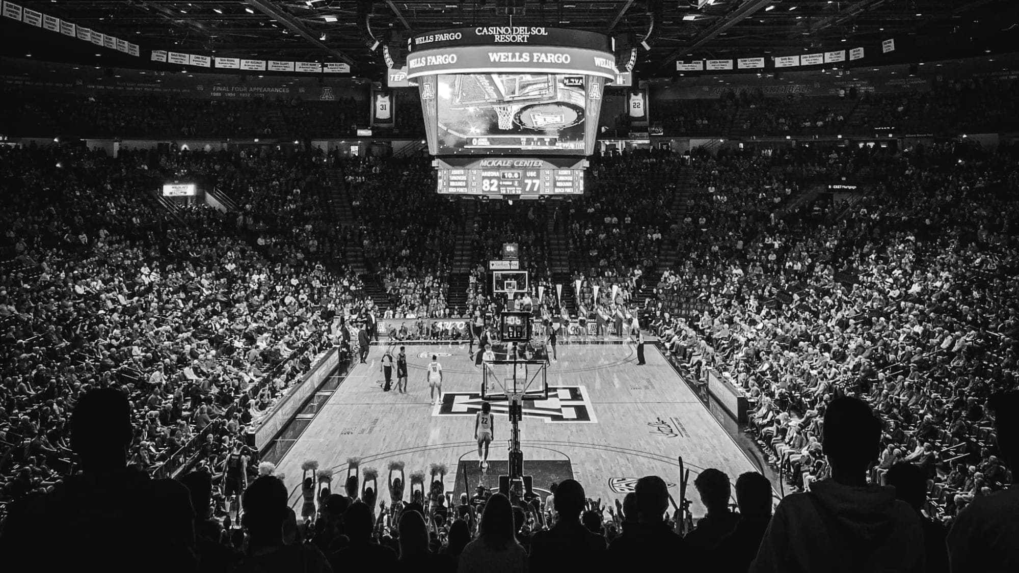 Black and white photograph looking down into a packed college basketball arena, every tier of seating full, with a game in progress on the court below.